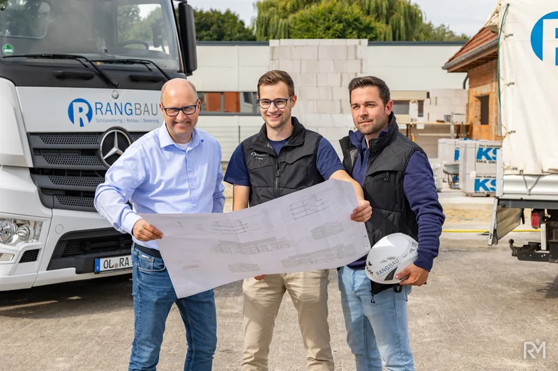 Drei Mitarbeiter mit Bauplan vor dem Firmen-LKW