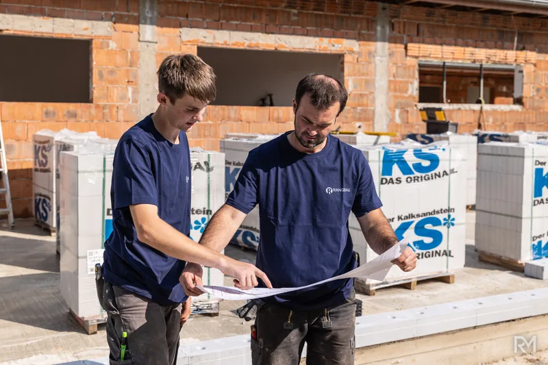 Zwei Handwerker vergleichen den Plan mit dem Rohbau