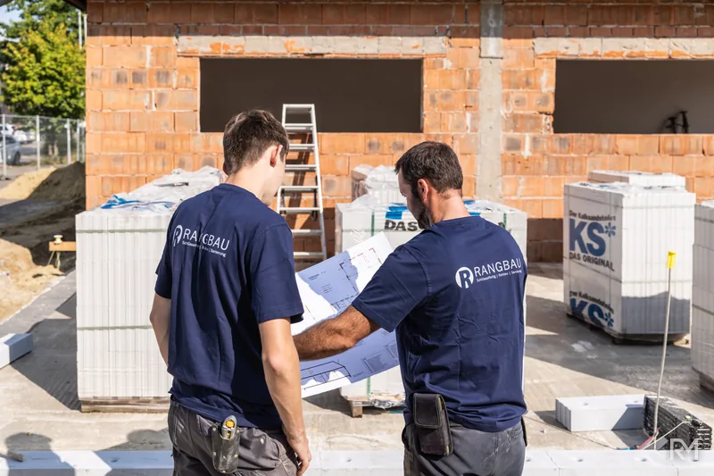 Zwei Handwerker am Steinstapel vor dem Rohbau